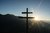 Holzkreuz vor Bergsilhouette bei Sonnenaufgang