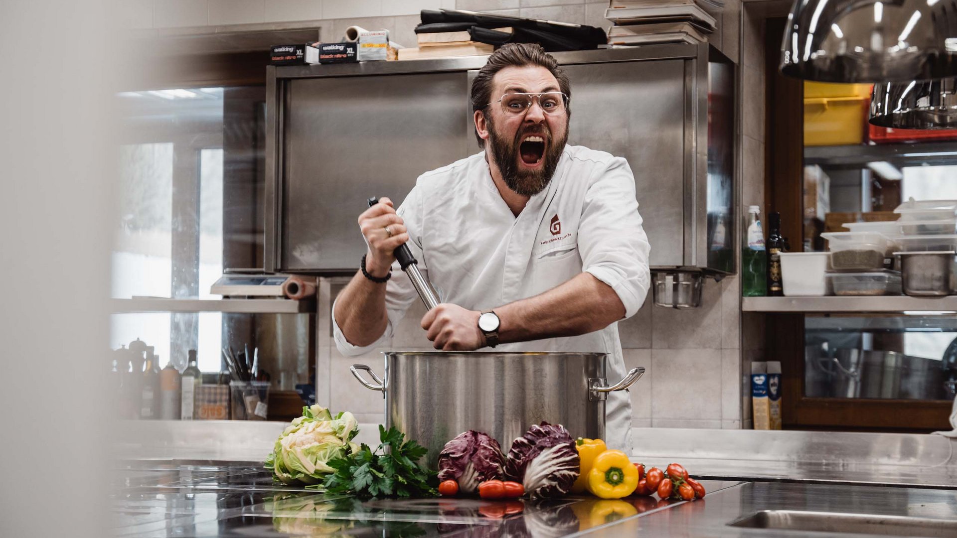 The Gassenhof gourmet cuisine Chef stirring large pot in professional kitchen with vegetables in front