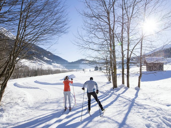 Urlaub in Ridnaun Zwei Personen beim Langlaufen im verschneiten Winterlandschaft mit Sonne und Bäumen