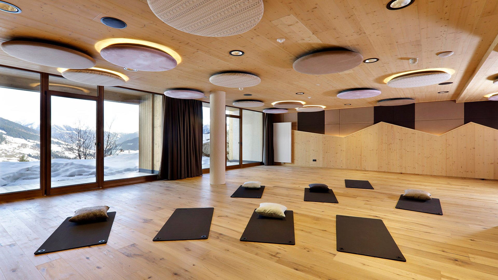 Fitness und Yoga Yoga-Raum mit Matten und Kissen vor großem Fenster mit Bergblick