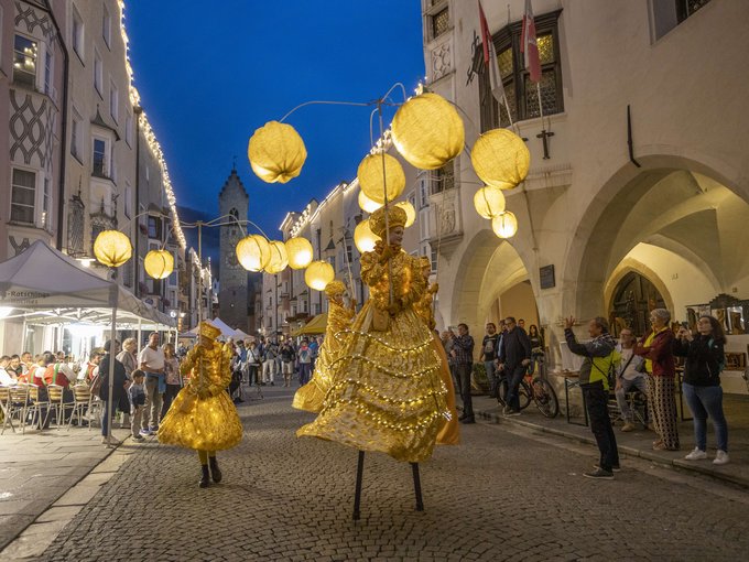 Laternenparty Sterzing Straßenszene bei Nacht mit Menschen in goldenen Kostümen und beleuchteten Kugeln