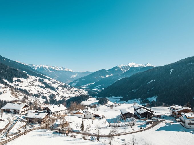 Nachhaltiger Urlaub Schneebedecktes Dorf in einem Tal mit Bergen und klarem blauem Himmel