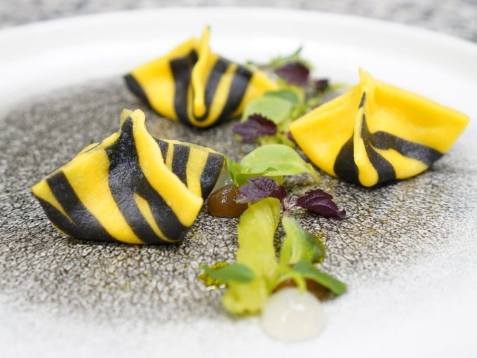 Una terra di stelle e cappelli Pasta ripiena gialla e nera con erbe su un piatto bianco