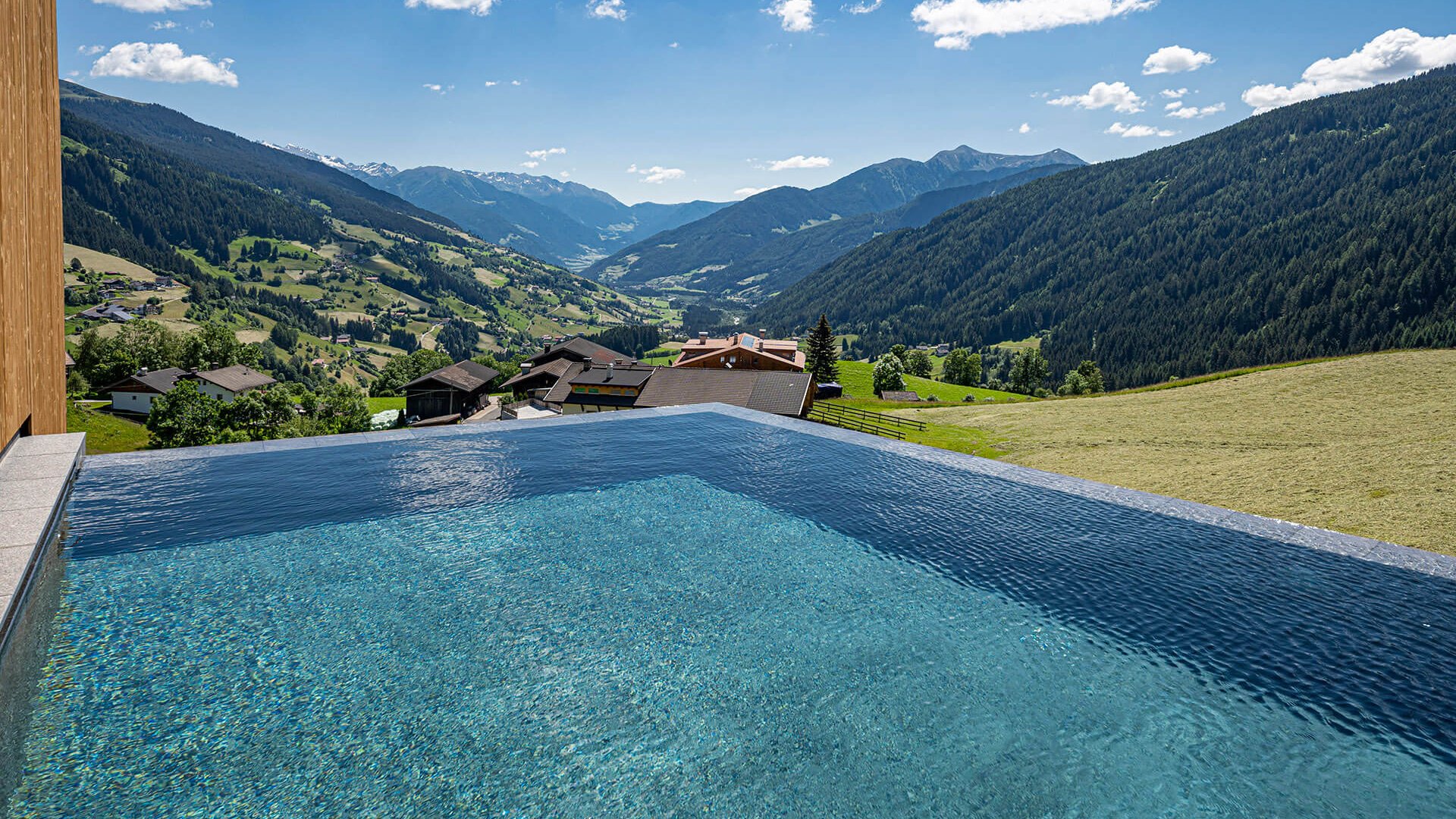 The best spot in the Ridnauntal valley Infinity pool overlooking mountains and houses in a sunny valley