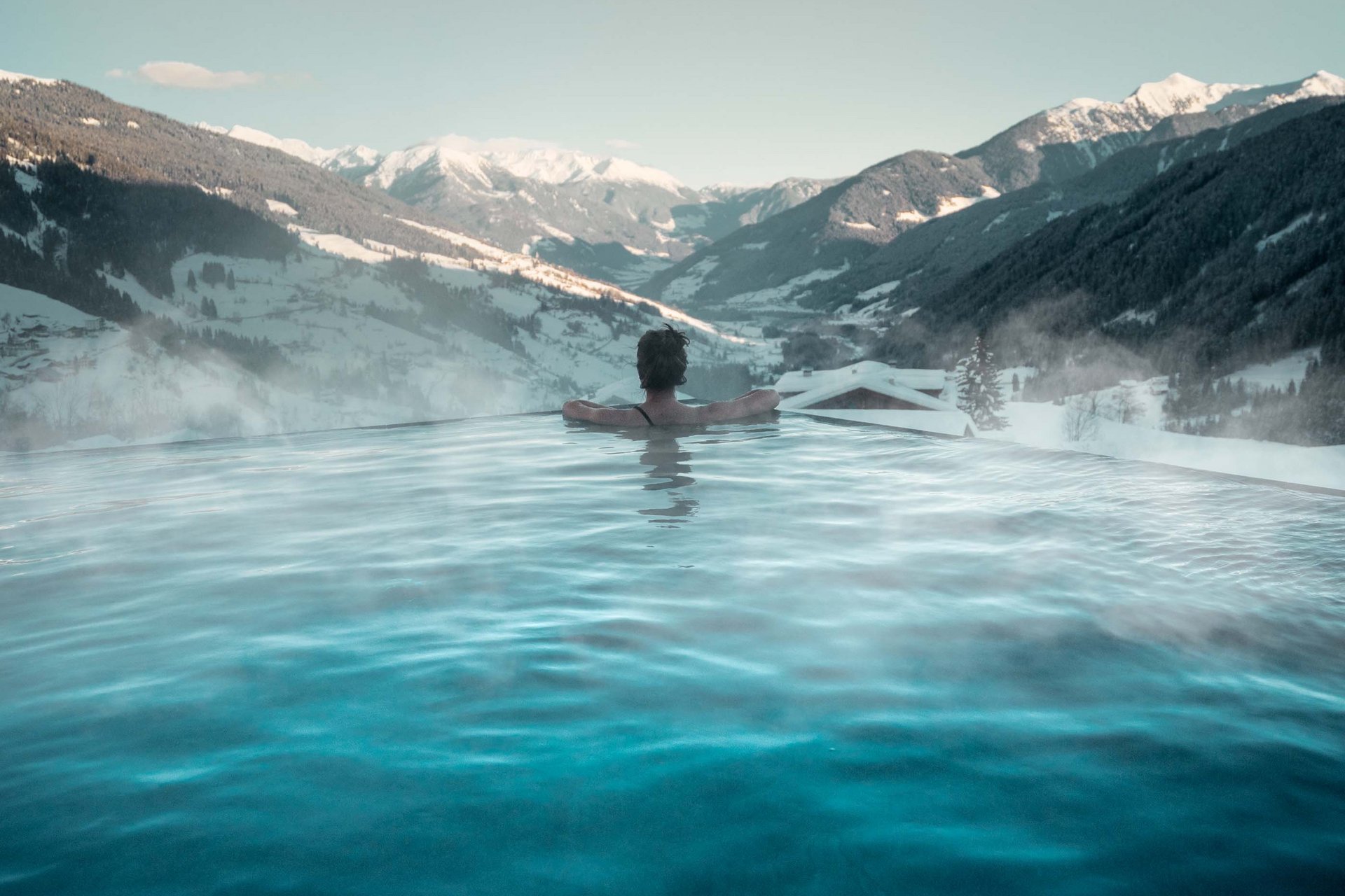 Urlaub anfragen Person im Außenpool mit Blick auf schneebedeckte Berge