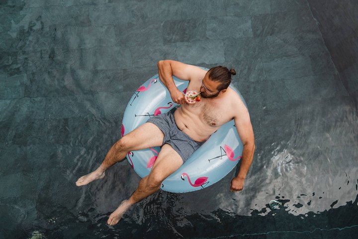 Arbeiten im Erlebnisort Gassenhof Mann entspannt im Pool auf Flamingo-Schwimmring mit Cocktail in der Hand