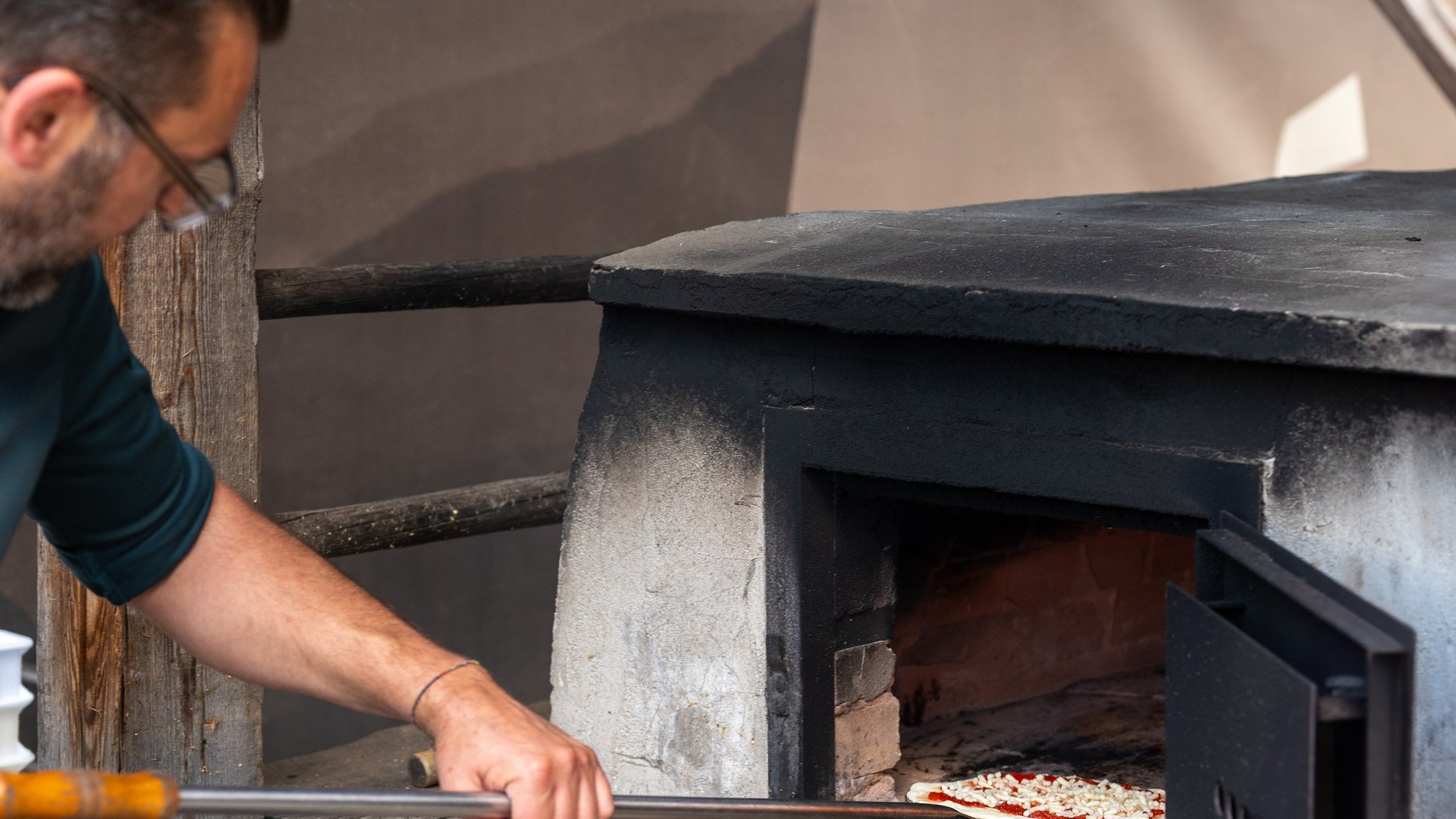 A place of experiences Man sliding a pizza into an oven with a pizza peel