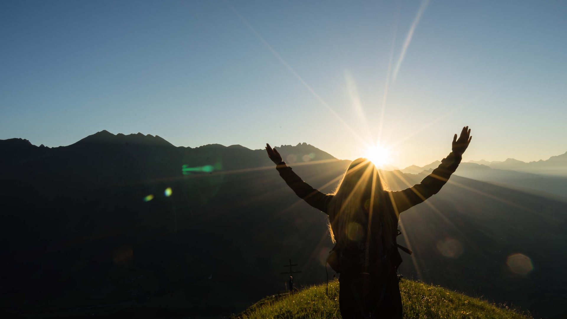 Summer experiences in South Tyrol Person standing on hill with raised arms at sunrise in front of mountains