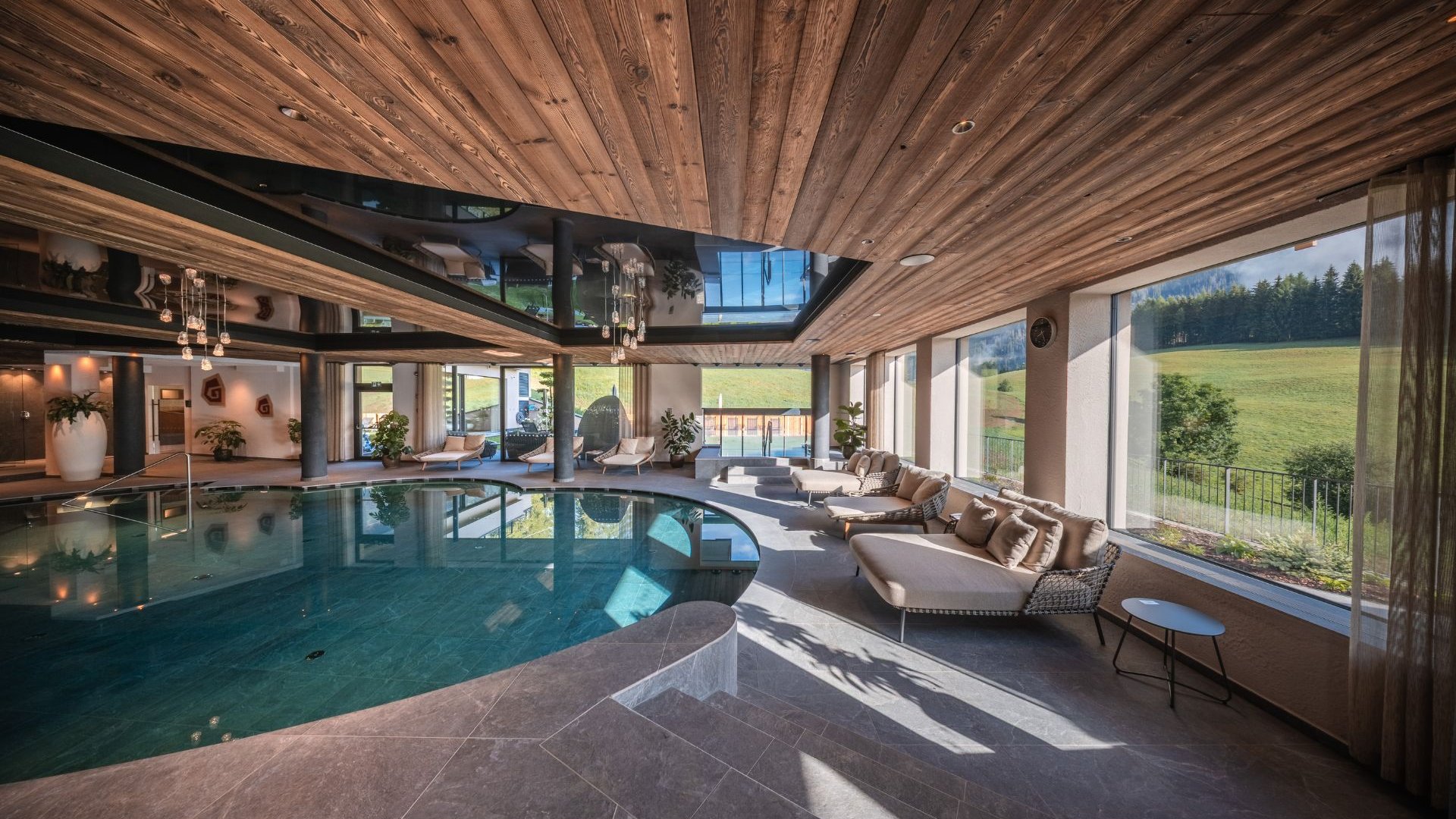 Gassenbadl: l’area wellness per famiglie Piscina coperta con lettini e grandi finestre affacciate su un prato verde