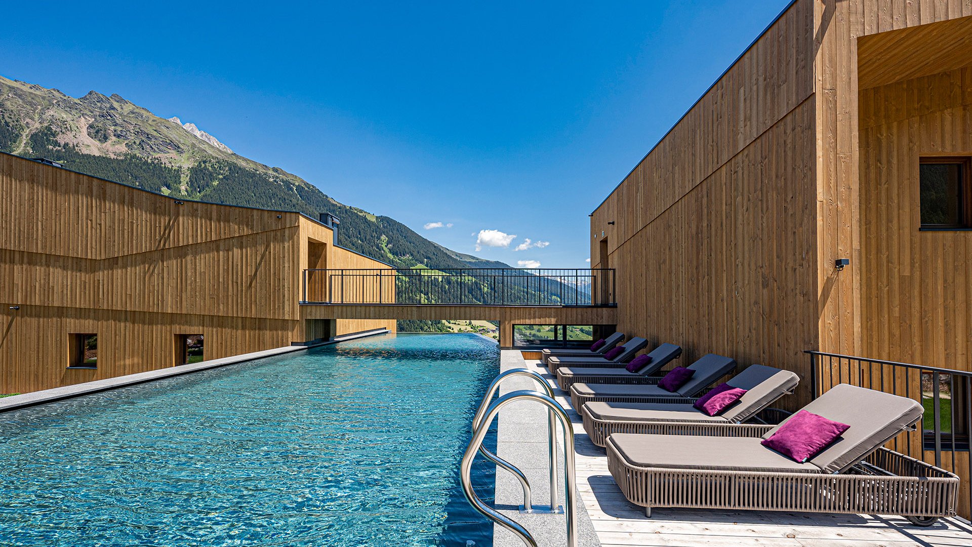 Hotel a Racines con centro benessere Piscina esterna con lettini e vista sulle montagne sotto un cielo sereno