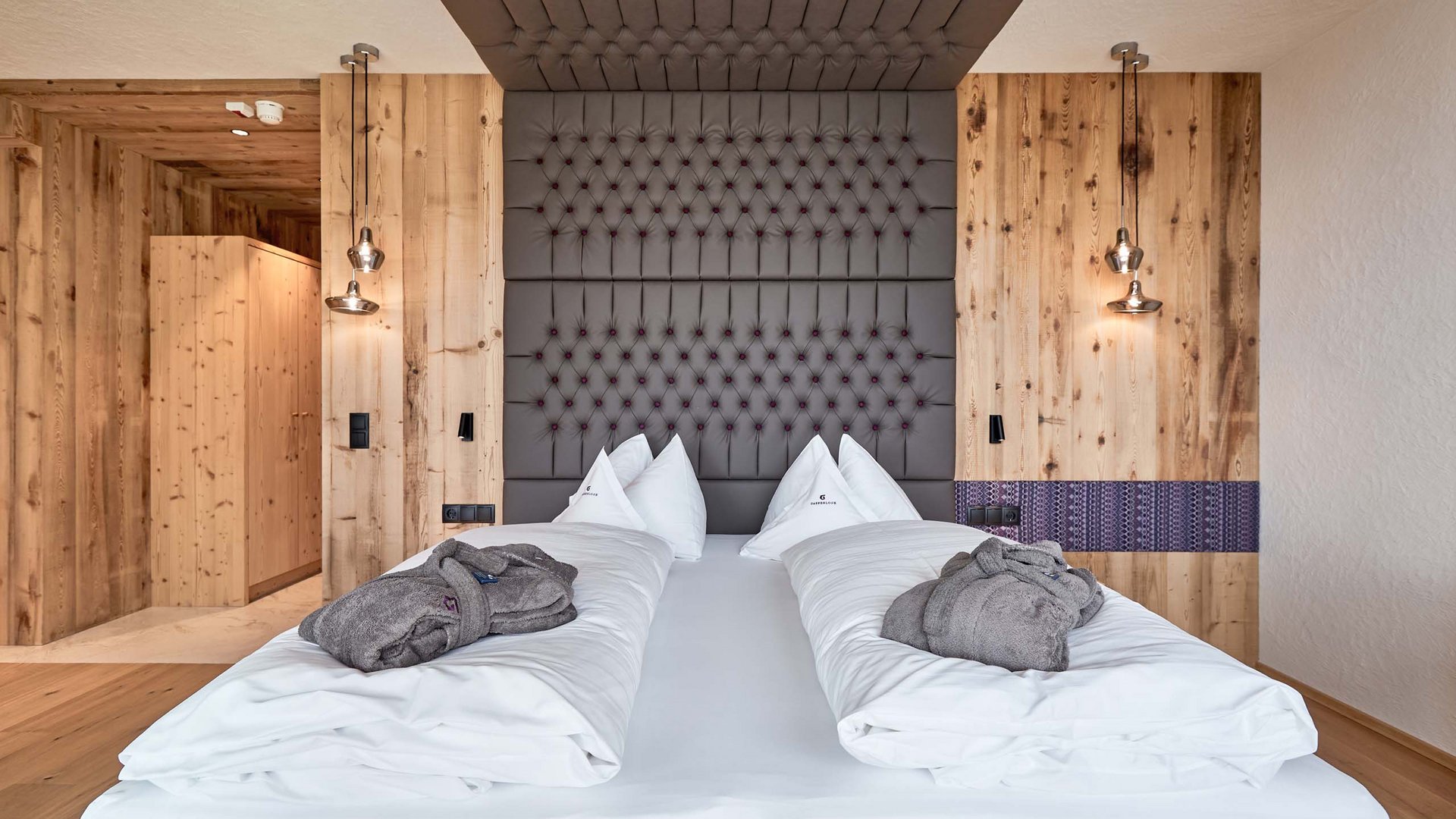 Inclusive services Modern hotel room with wooden walls, large upholstered bed, and gray bathrobes