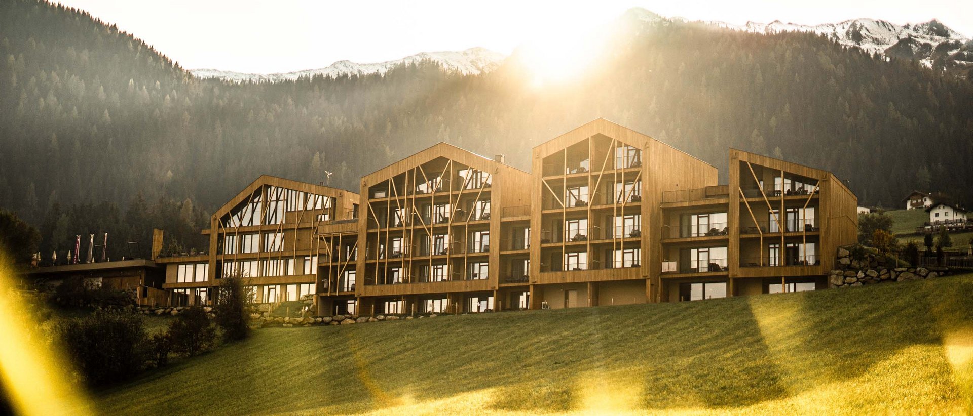 Urlaub anfragen Modernes Holzgebäude vor bewaldeten Bergen im Sonnenlicht