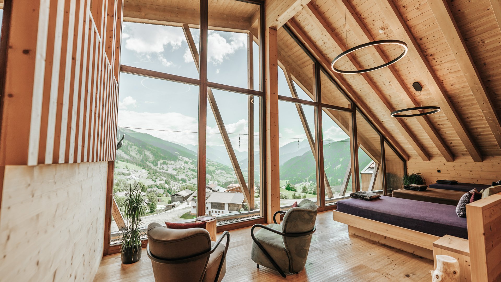 L’area wellness riservata agli adulti Camera in legno con letto e poltrone davanti a grandi finestre con vista sulle montagne