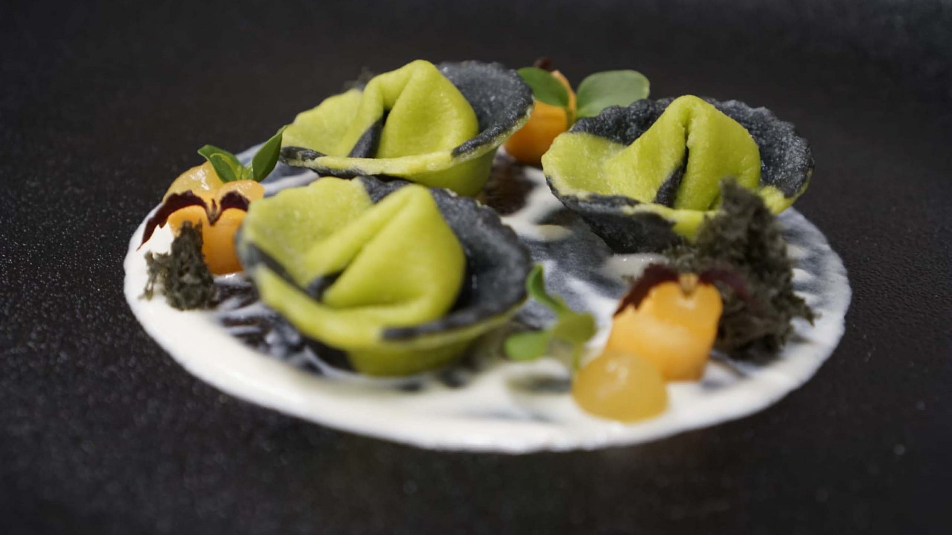Der Erlebnisort Gassenhof Grüne und schwarze gefüllte Pasta kunstvoll auf weißer Sauce angerichtet