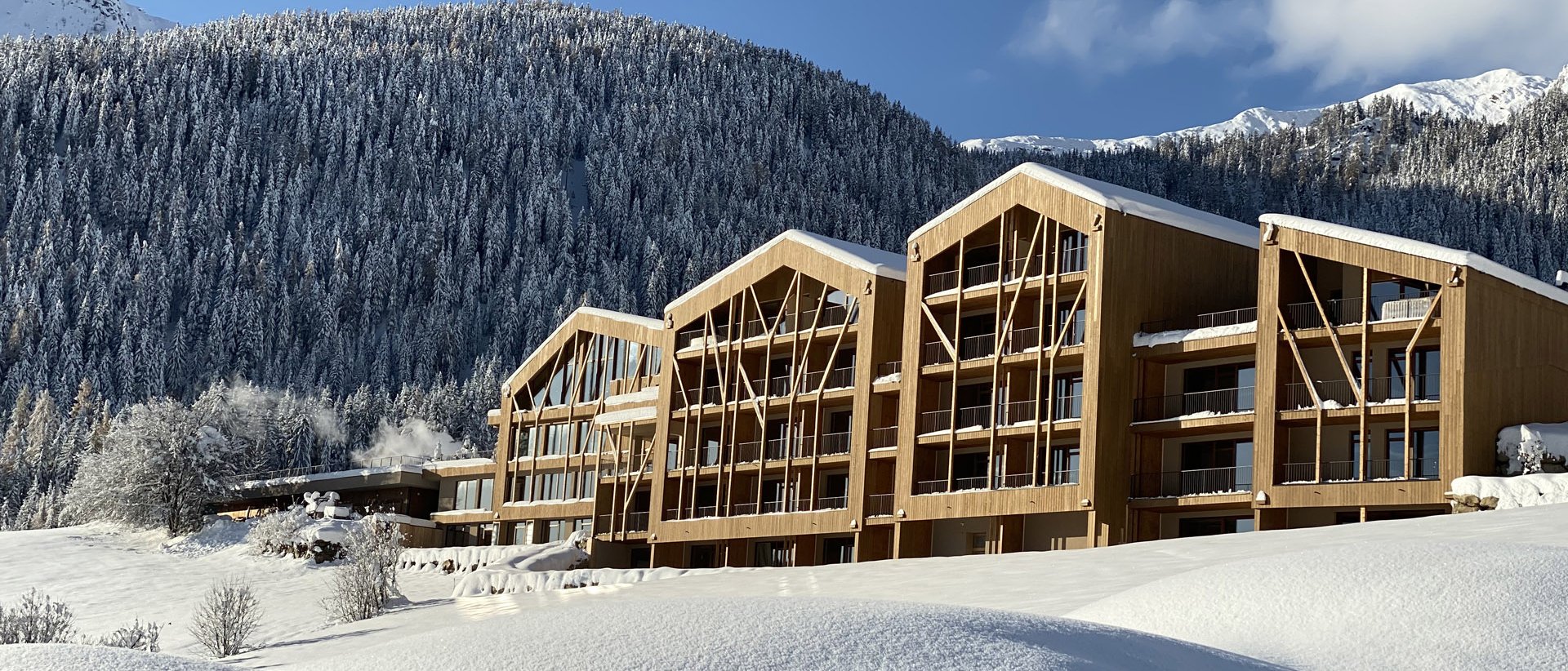 Urlaub anfragen Moderne Holzhäuser im verschneiten Bergland unter blauem Himmel