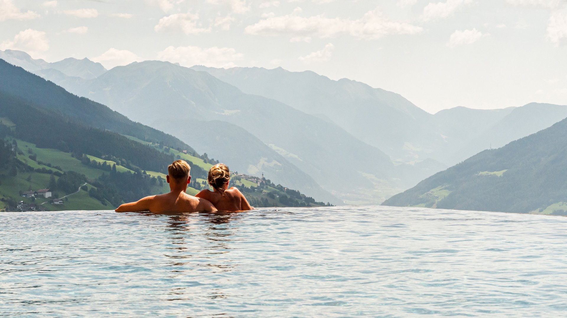 Der Erlebnisort Gassenhof Paar entspannt im Infinity-Pool mit Blick auf Berglandschaft