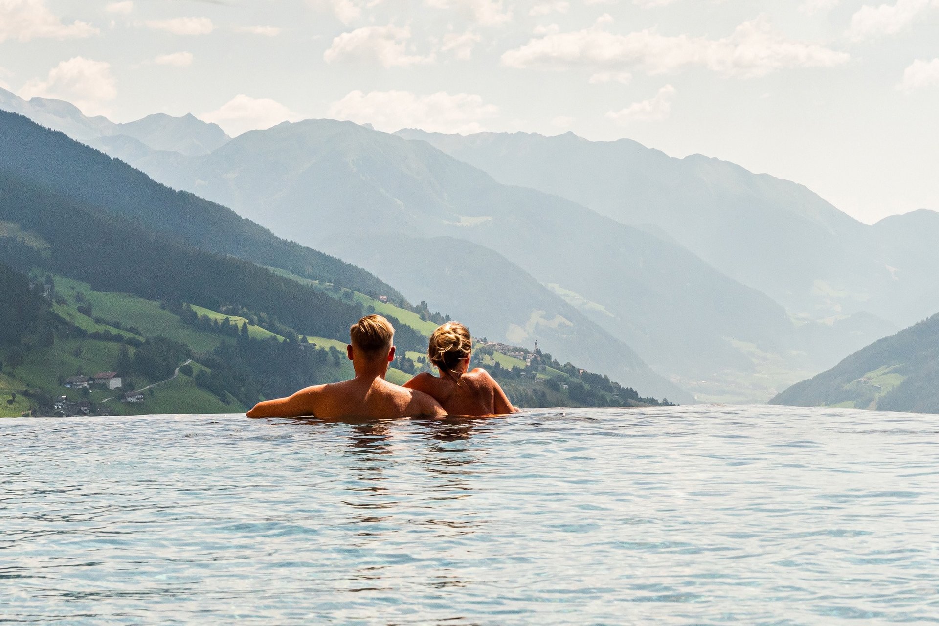 Urlaub anfragen Paar entspannt im Infinity-Pool mit Blick auf Berglandschaft