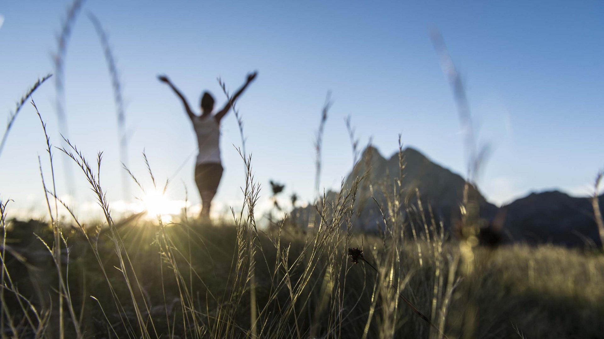 Wanderhotel Persona con le braccia alzate in un campo al tramonto davanti alle montagne