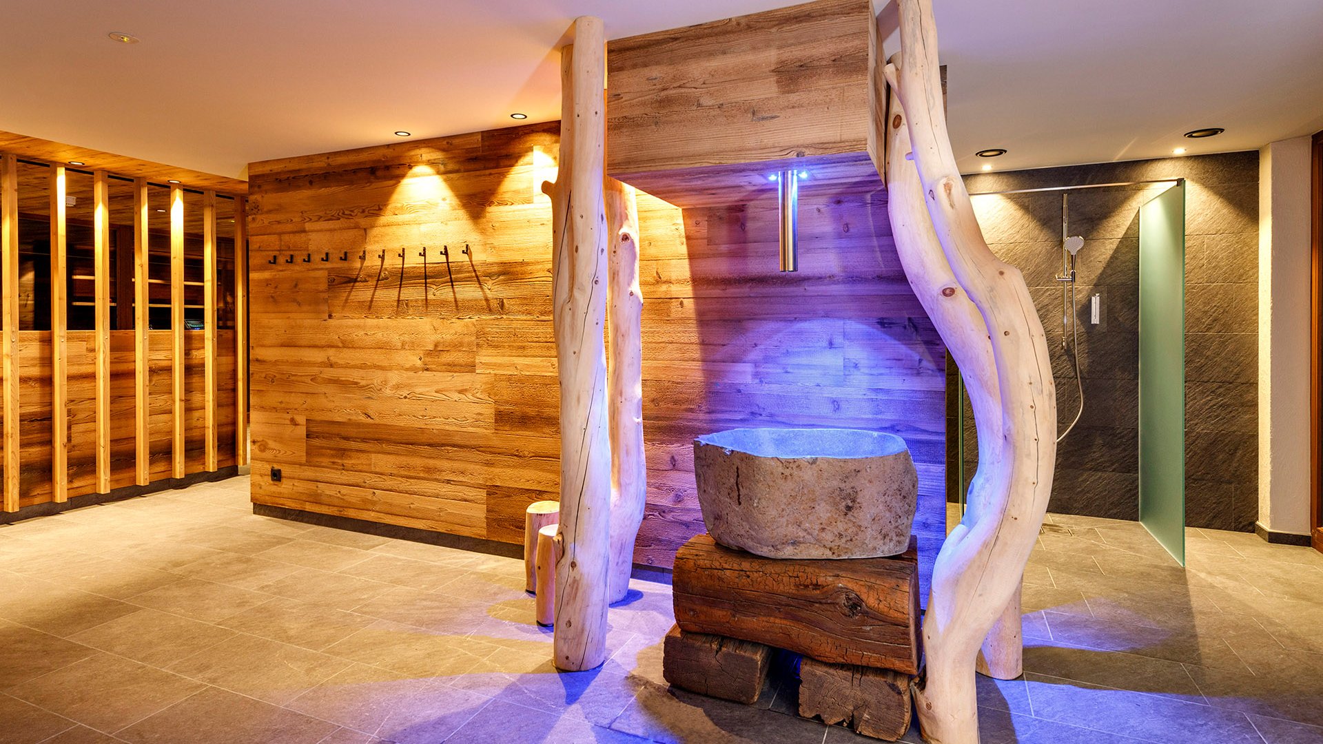 Hotel a Racines con centro benessere Area benessere moderna con rivestimenti in legno e fontana di pietra con luce blu