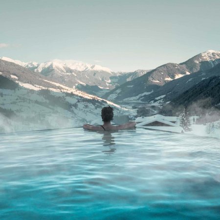 Wellness im Erlebnishotel Gassenhof Person entspannt im beheizten Pool mit Blick auf schneebedeckte Berge