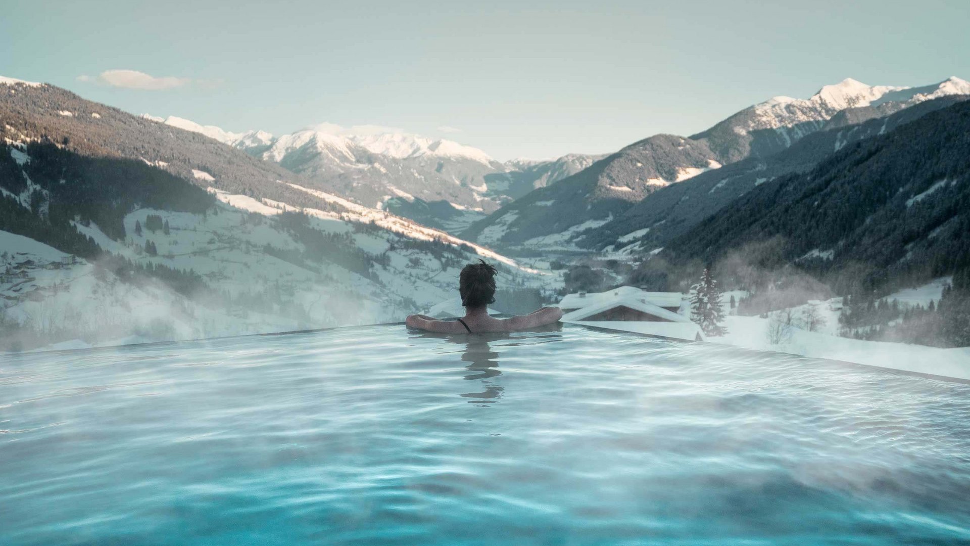 Der Erlebnisort Gassenhof Person entspannt im beheizten Pool mit Blick auf schneebedeckte Berge