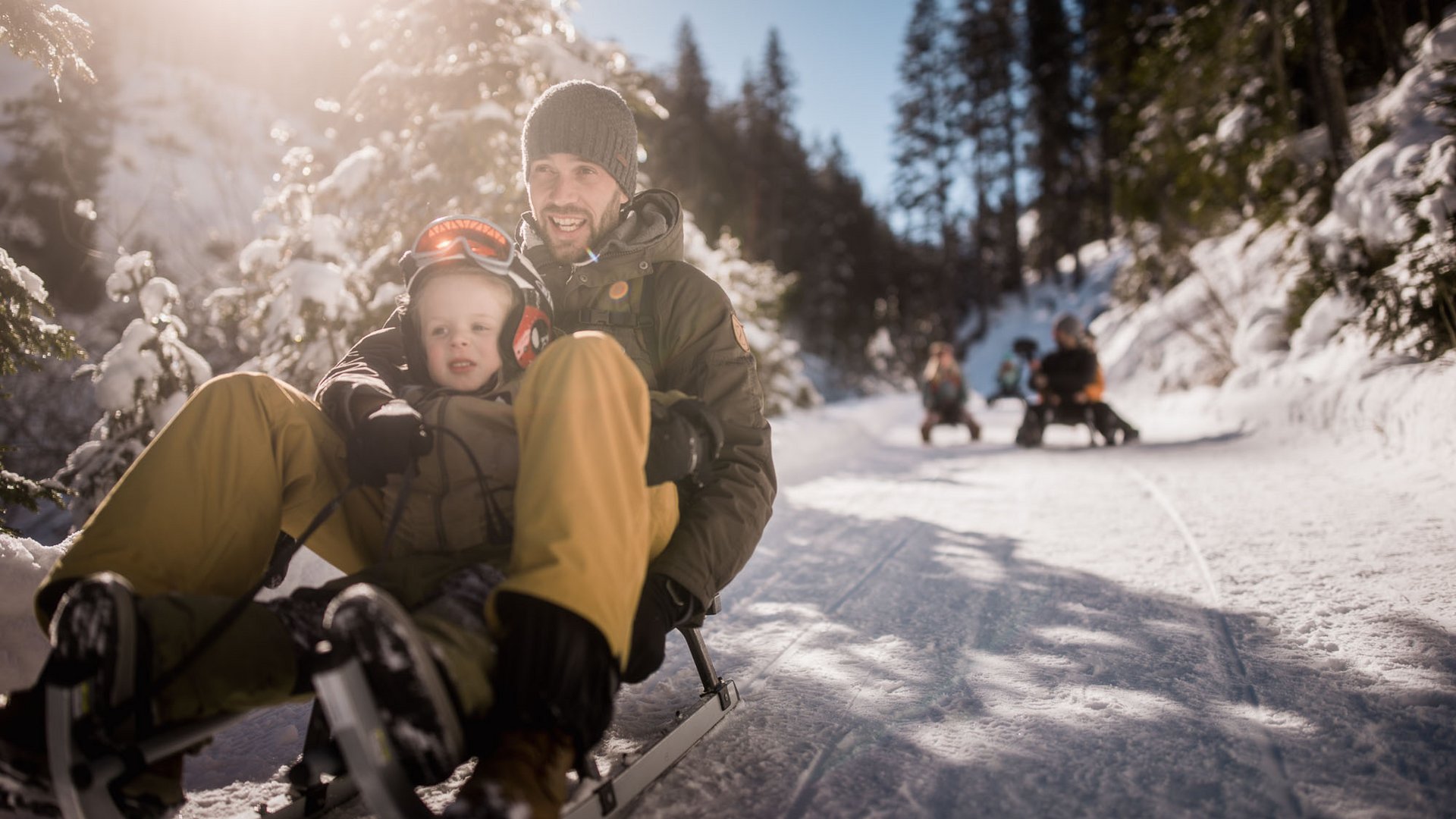Aktivitäten mit Kindern im Ridnauntal Mann und Kind fahren auf einem Schlitten durch einen verschneiten Wald