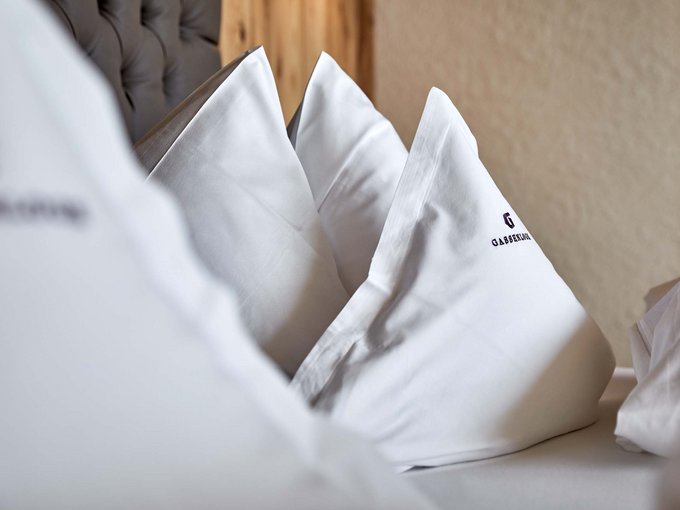 Zimmer und Suiten Drei weiße Kissen auf einem Bett mit einem Kopfteil im Hintergrund.